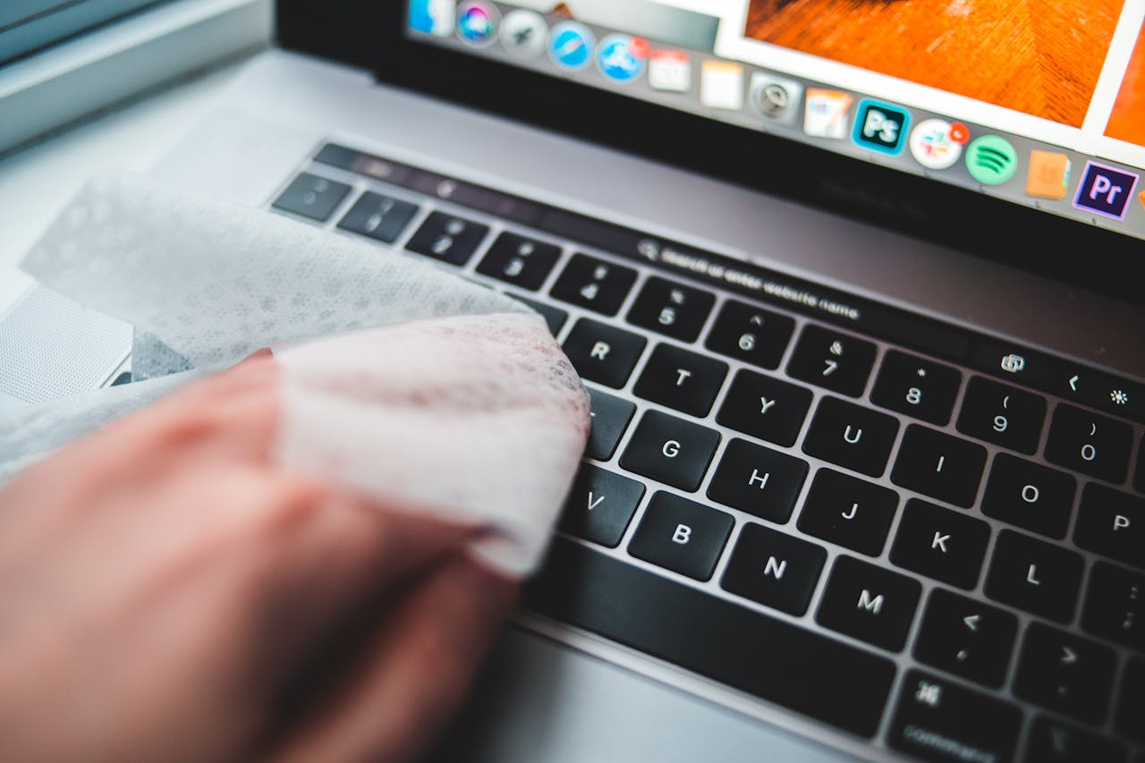 about-us Person cleaning a laptop keyboard using disinfectant wipes for hygiene.
